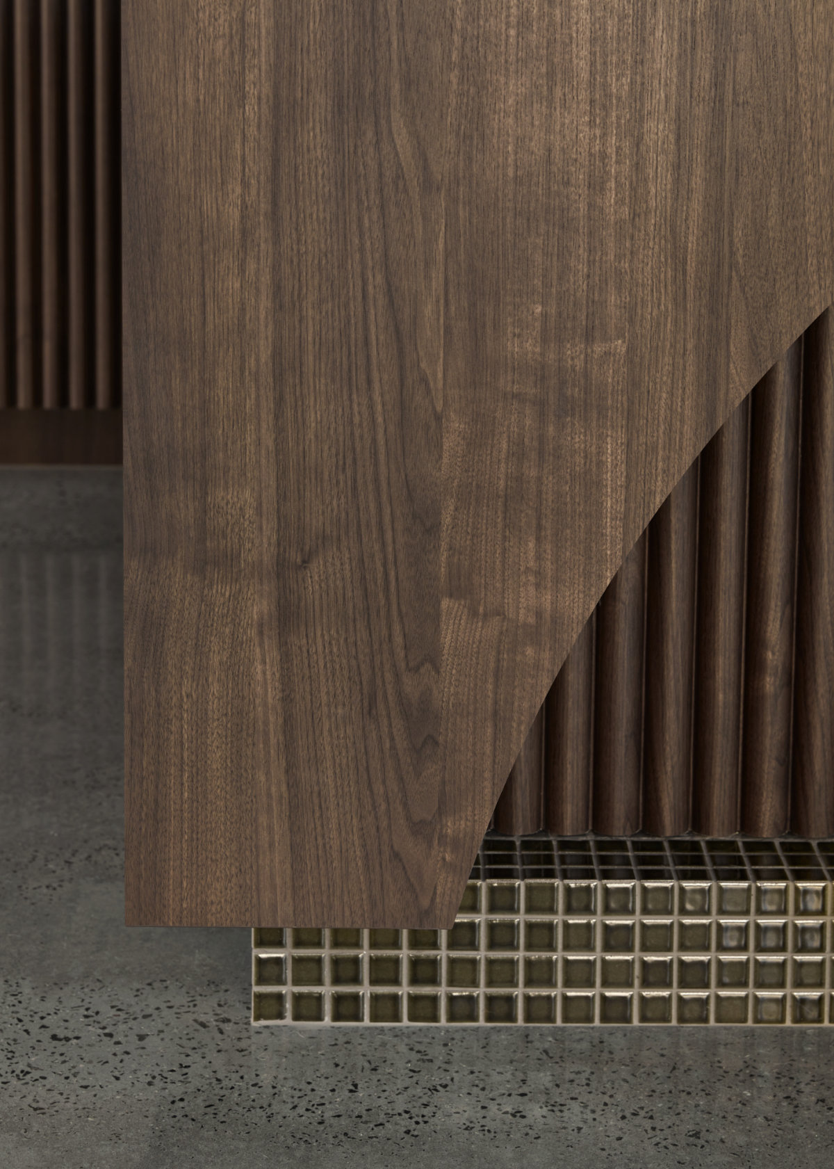 Close-up of details on the base of the kitchen bench. A curved timber panel overlays an accordion-like wooden surface. Dark olive tiles line the base of the bench.
