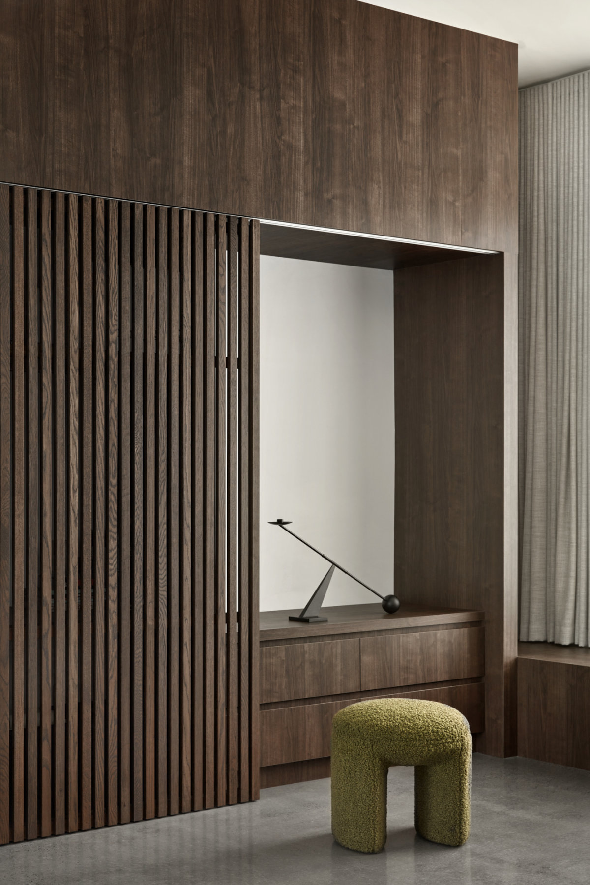 A fuzzy olive-coloured stool in front of floor-to-ceiling timber cabinetry.