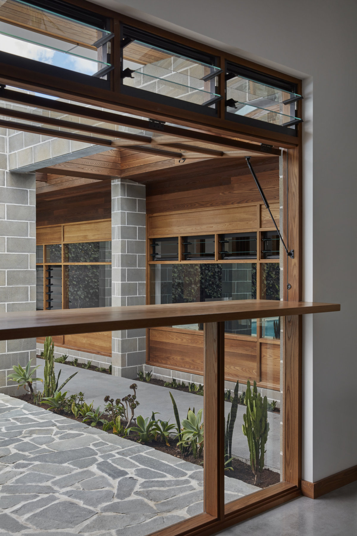 Teak window frame that incorporates a bench top. The window above the bench top opens out vertically providing a clear view in to the backyard.